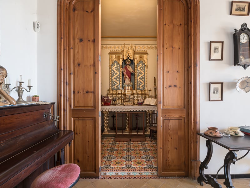 Vue à travers des portes en bois sur une petite chapelle privée ornée à côté d'un piano droit.