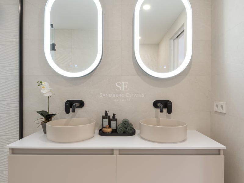 Salle de bain moderne avec deux vasques à poser, robinetterie noire et miroirs ovales rétroéclairés sur mur beige.