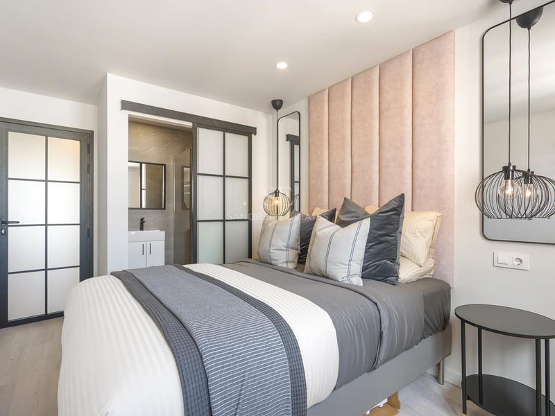 Zeitgenössisches Schlafzimmer mit rosa Samtkopfteil, industriellen Glastüren und Blick auf das En-Suite-Bad.