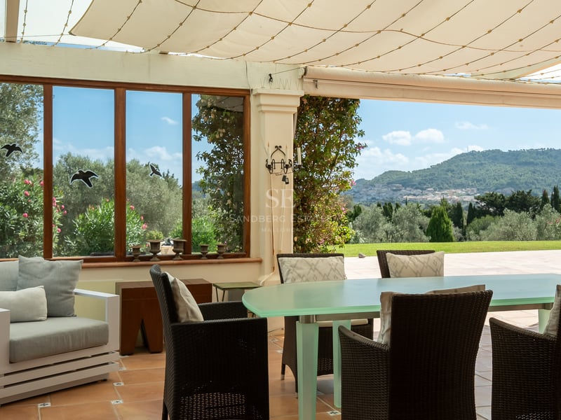 Terrasse extérieure couverte avec grande table à manger, chaises en osier et vue sur les collines et montagnes.