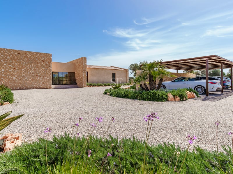 Moderne Villa mit Natursteinwänden, großer Kiesauffahrt und Carport unter strahlend blauem Himmel.