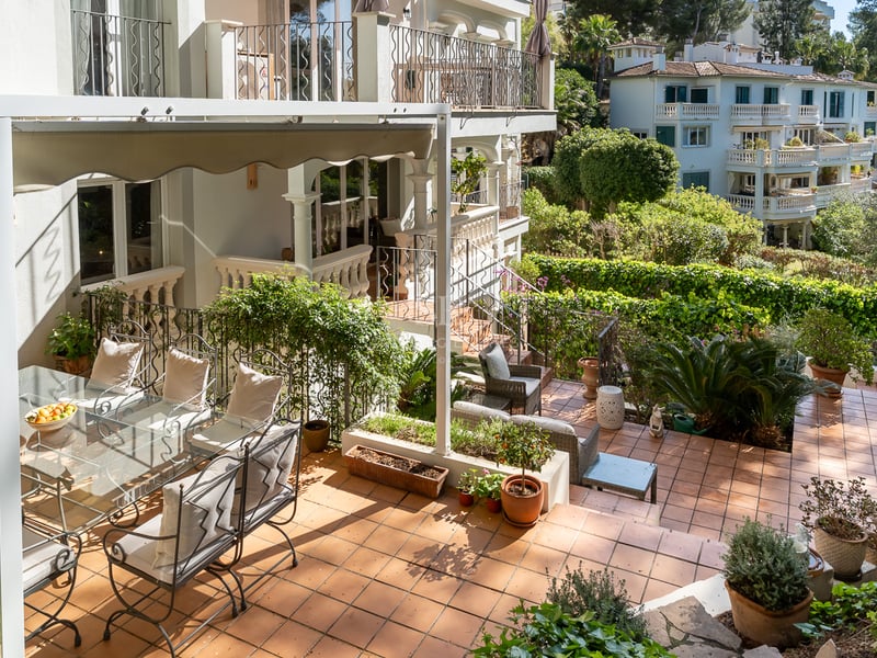 Sun-drenched Mediterranean terrace with terracotta tiles, wrought iron dining set under a white awning, and lush greenery.