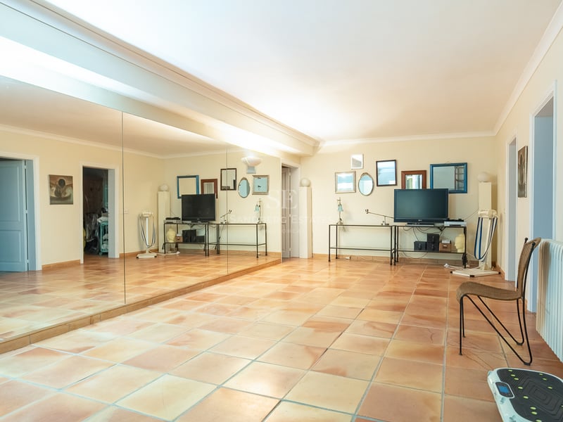 Grande pièce avec sol en terre cuite, un mur de miroirs et du matériel de fitness dans une villa de luxe.