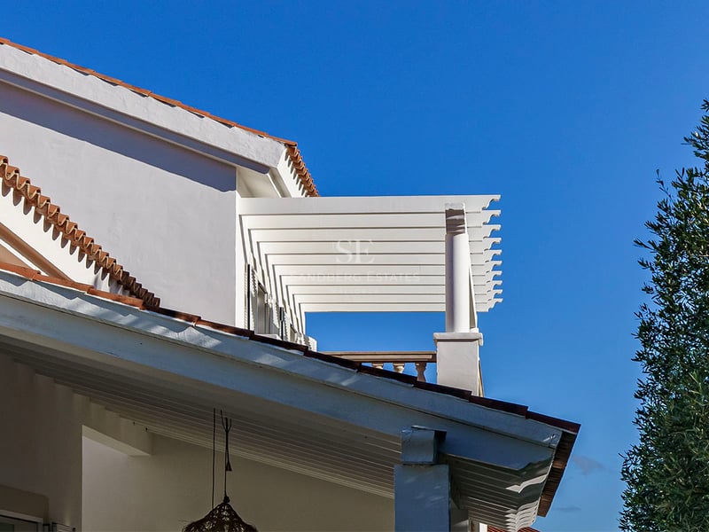 Vit villafasad med träpergola, terrakottatak och klarblå himmel på Costa del Sol.