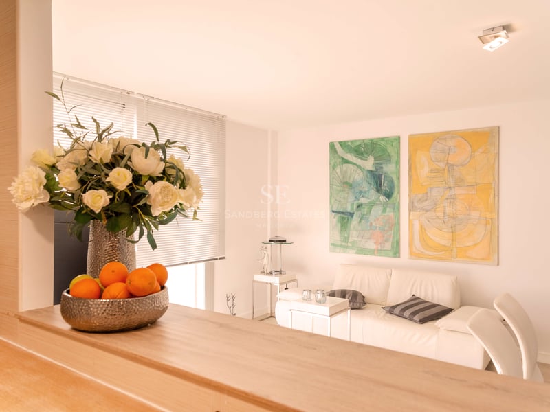 Helles Wohnzimmer mit weißem Ledersofa, abstrakten Gemälden und einer Holztheke mit Blumendekor.