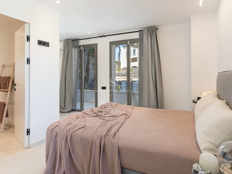 Modernt sovrum med grå stoppad säng, lila pläd, fönster från golv till tak och ingång till eget badrum.