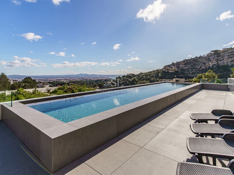 Piscine à débordement sur une terrasse en pierre avec chaises longues surplombant la vallée et la ville.