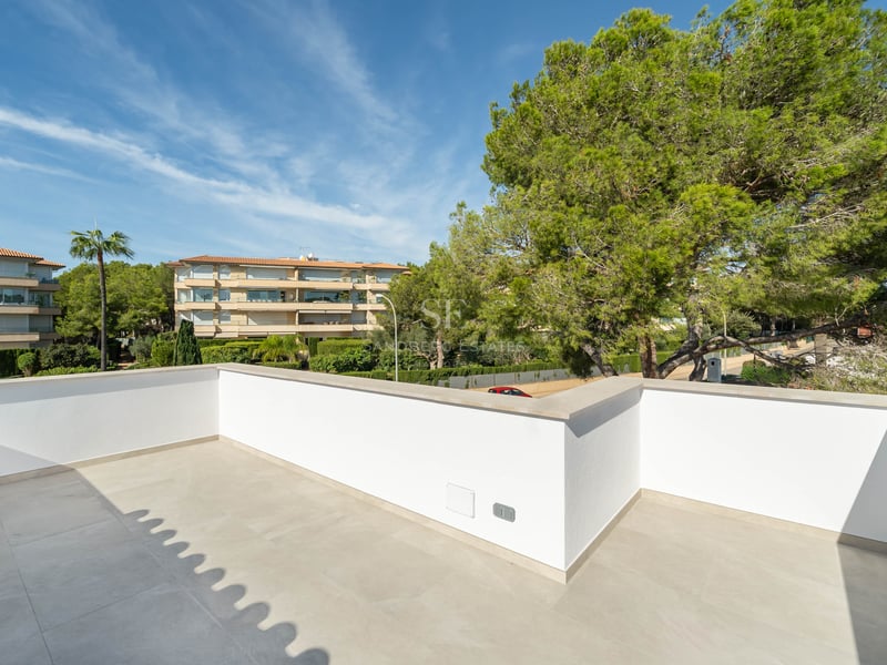 Grande terrasse moderne avec murs blancs et sol en pierre claire, donnant sur des pins luxuriants et des bâtiments.