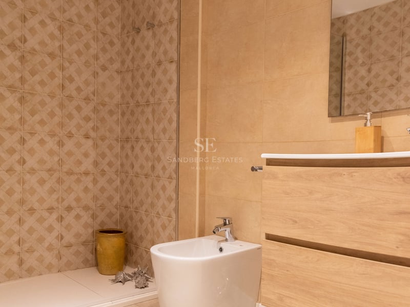 Zeitgenössisches Badezimmer mit sandfarbenen Fliesen, begehbarer Dusche, schwebendem Holzwaschtisch und weißem Bidet.