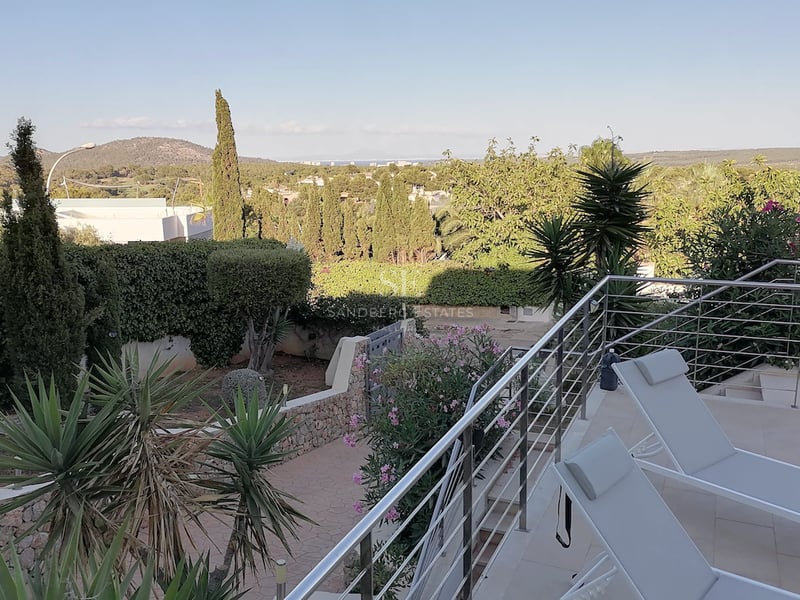 Une terrasse ensoleillée avec des chaises longues modernes et des garde-corps en acier inoxydable surplombant un jardin.