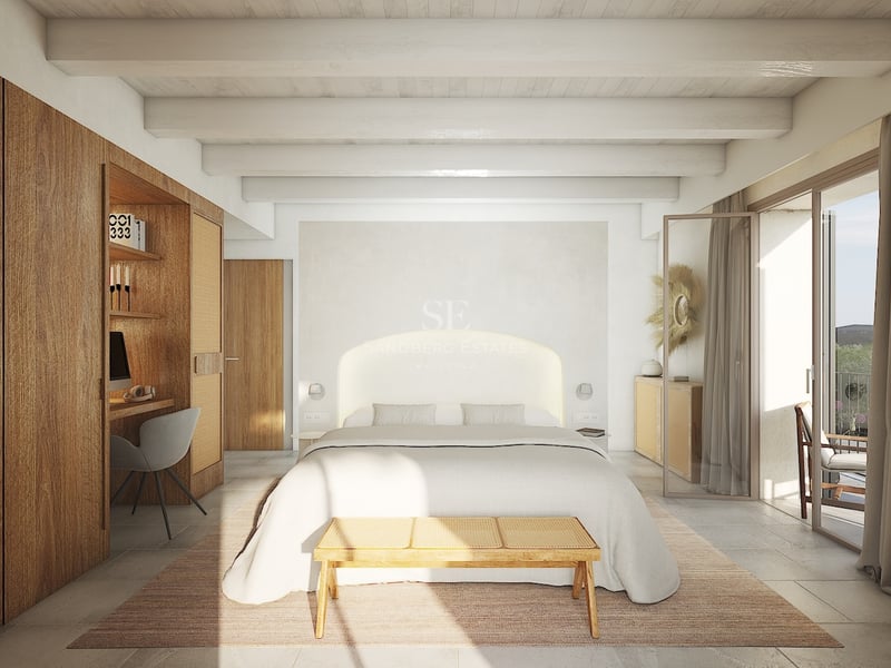 Chambre lumineuse avec poutres blanches, armoires en bois intégrées avec bureau, grand lit et accès au balcon.