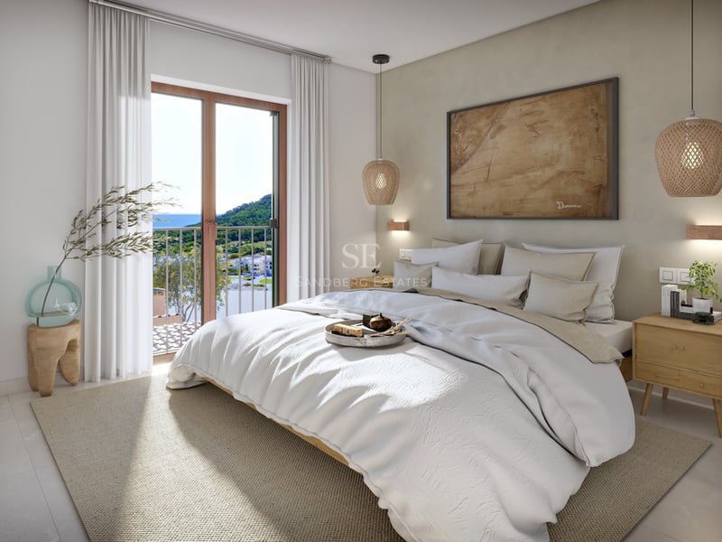 Bright bedroom featuring a white bed, wicker lamps, and a balcony with mountain and sea views.