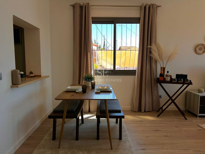 Wooden dining table with benches, neutral curtains, and pampas grass decor by a window.