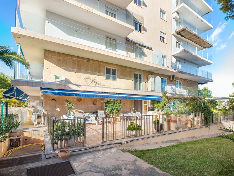 Mehrstöckiges Wohngebäude mit Natursteinverkleidung, Glasbalkonen und großer Terrasse mit blauer Markise.