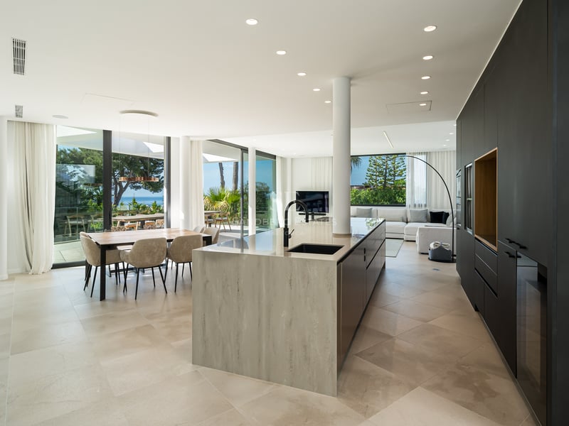 Cuisine ouverte avec grand îlot en pierre, armoires sombres et coin repas avec baies vitrées toute hauteur.