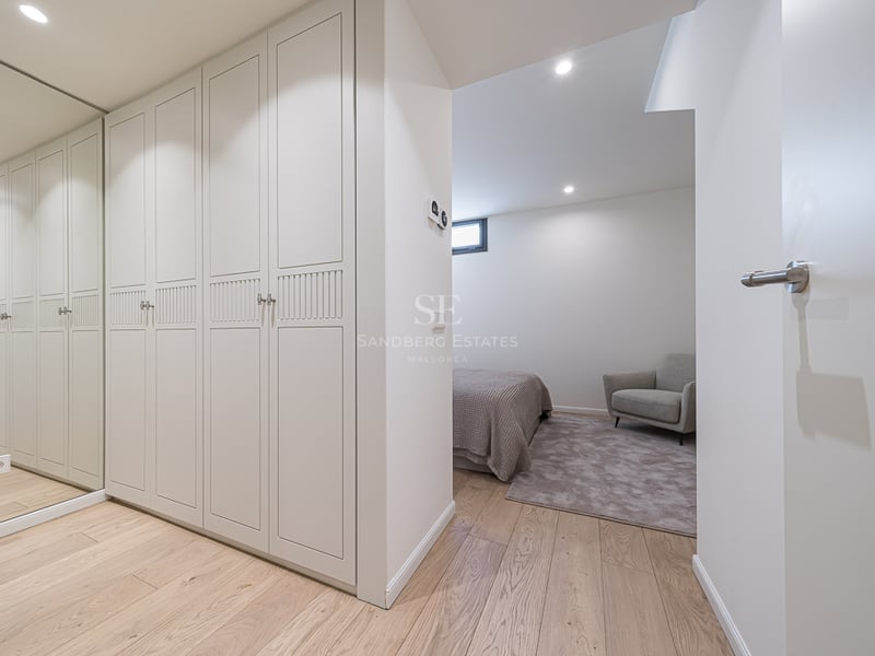 Cream lacquered built-in wardrobes with a full-length mirror and light oak flooring leading into a bedroom.