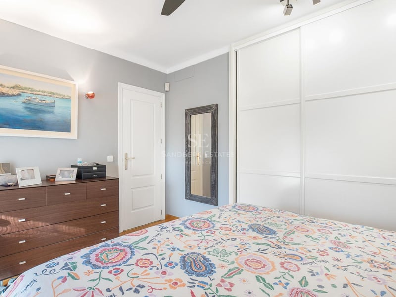 Helles Gästezimmer mit großen weißen Schiebetürenschränken, dunkler Holzkommode und geblümter Bettwäsche.