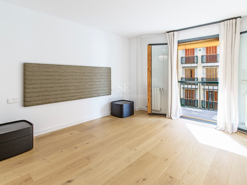 Chambre moderne avec parquet en bois clair, tête de lit murale texturée et balcon baigné de lumière naturelle.