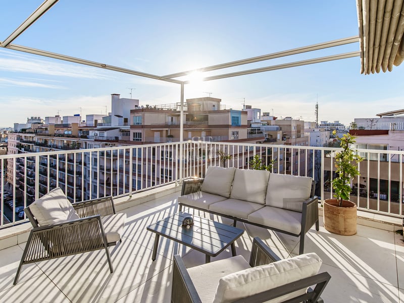 Terrasse ensoleillée avec mobilier gris moderne, balustrades blanches et vue imprenable sur la ville.