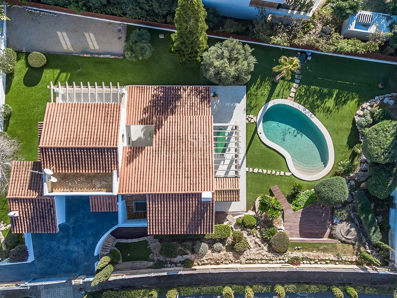 Fågelperspektiv av en lyxvilla med tegeltak, njurformad pool och välskötta trädgårdar.