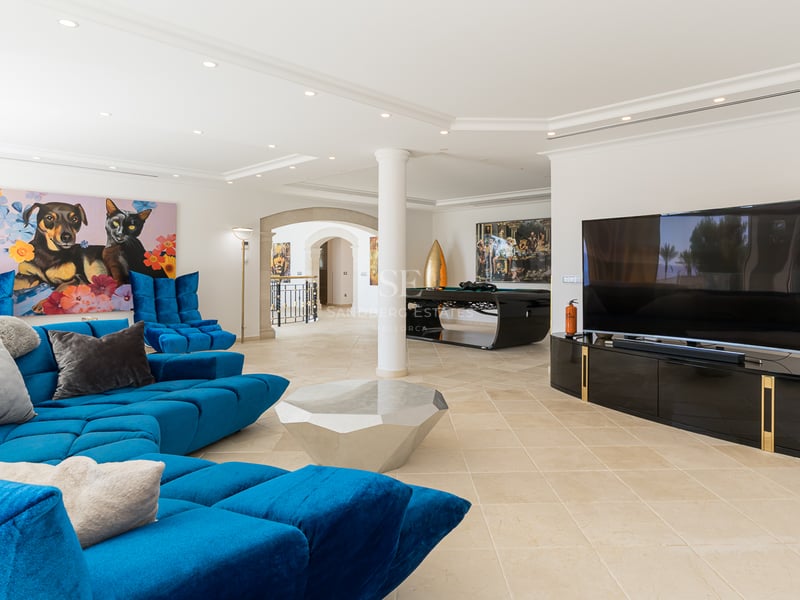 Heller Wohnraum mit blauem Samtsofa, geometrischem Couchtisch und Billardtisch im Hintergrund.