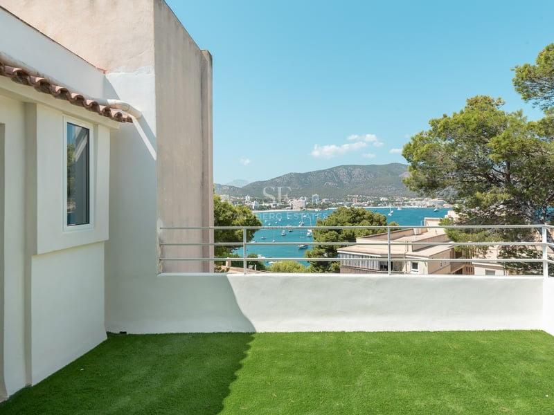 Terrasse avec gazon artificiel et garde-corps blanc surplombant une baie bleue avec des yachts et des montagnes.