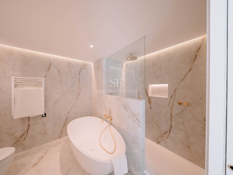 Salle de bain élégante avec baignoire îlot, douche à l'italienne et murs en marbre avec robinetterie dorée.