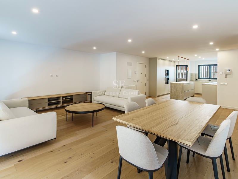 Pièce moderne spacieuse avec canapés blancs, grande table à manger en bois et cuisine contemporaine en arrière-plan.