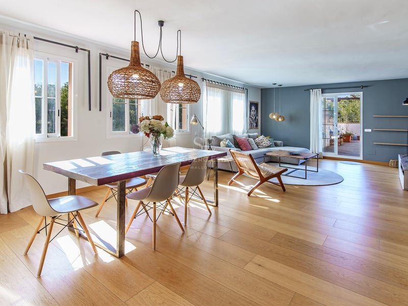 Ljust vardagsrum med ekparkett, rustikt matbord under flätade lampor och utgång till terrassen.