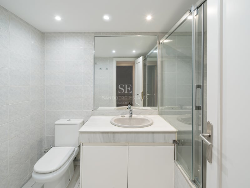 Ljust badrum med vit marmorkommod, duschvägg i glas och ljusgrått väggkakel.