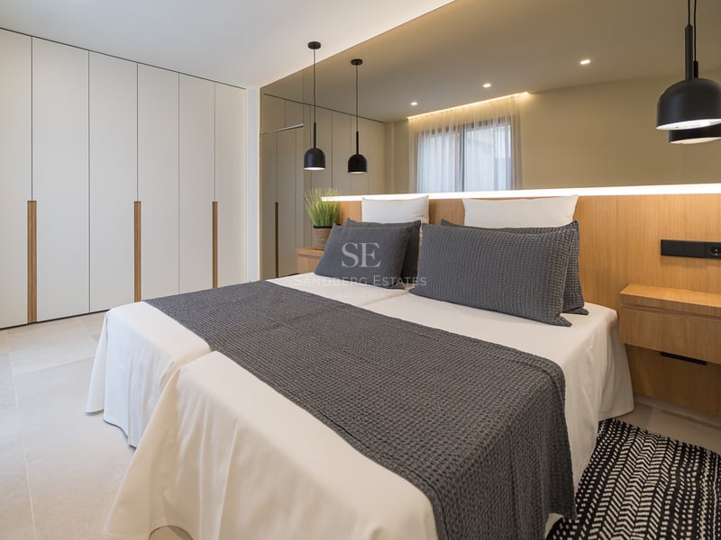 Chambre moderne avec lits jumeaux, placards blancs du sol au plafond, tête de lit en chêne et grand miroir mural.