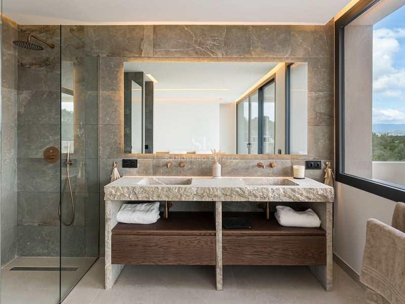 Luxuriöses Badezimmer mit Doppelwaschtisch aus Naturstein, hinterleuchtetem Spiegel und dunklen Holzakzenten.