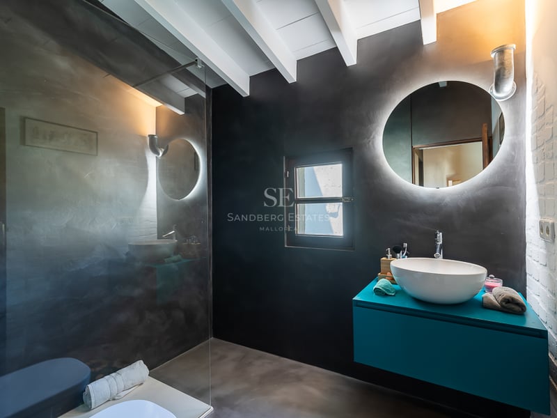 Salle de bains contemporaine avec murs en béton ciré anthracite, meuble vasque turquoise et miroir rond rétroéclairé.