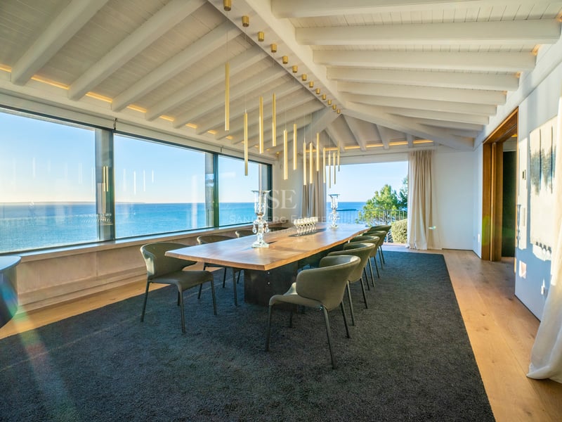 Luxuriöses Esszimmer mit Massivholztisch, Designerstühlen und großen Fensterfronten mit Blick auf das Mittelmeer.
