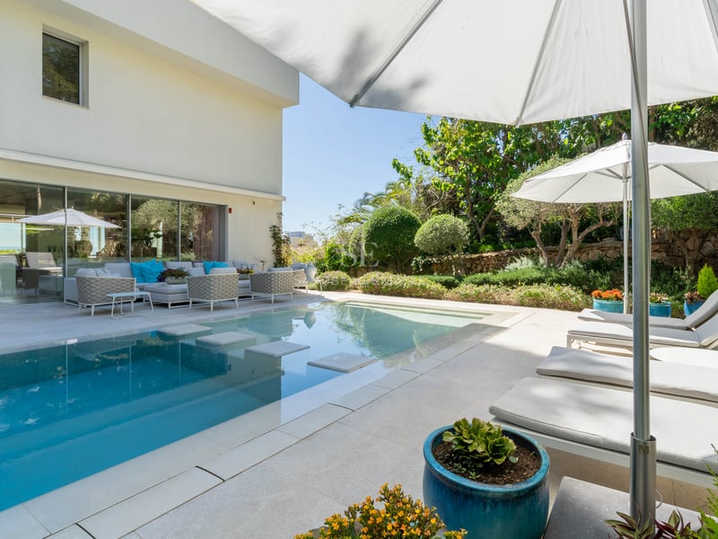 Eleganter Außenpool mit Trittsteinen, weiße Natursteinterrasse, Sonnenliegen und üppige Gartenbepflanzung.