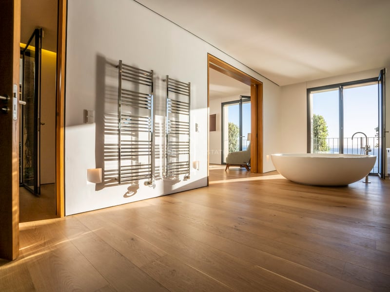 Minimalistisches Master-Bad mit Eichenparkett, ovaler freistehender Badewanne, verchromten Handtuchwärmern und Meerblick.