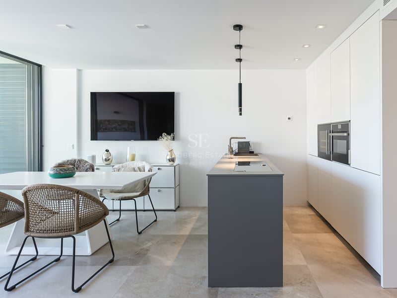 Moderne weiße Küche mit grauer Insel, Esstisch und bodentiefen Fenstern mit Blick auf das Mittelmeer.