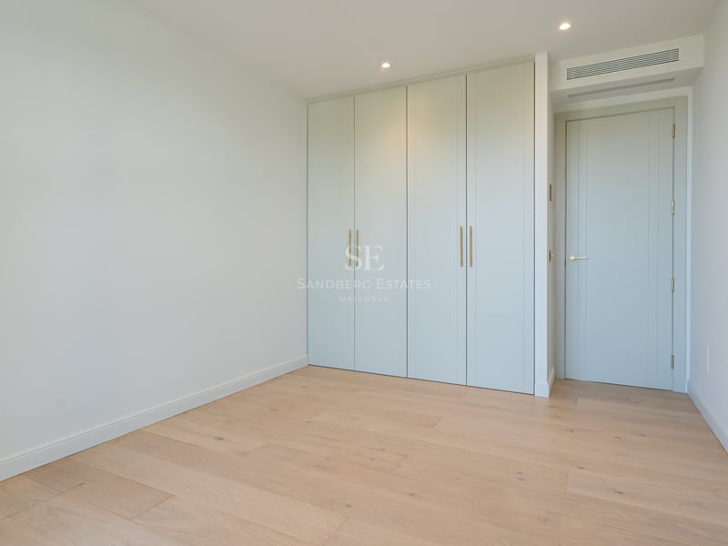 Empty room featuring light oak flooring, sage green built-in wardrobes, and minimalist white walls.