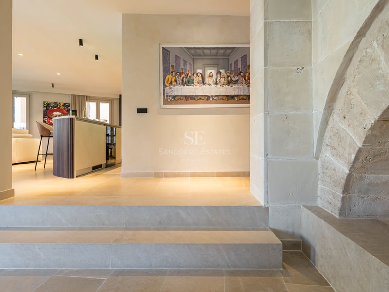 Intérieur de luxe avec une grande arche en pierre, des marches et un îlot de cuisine moderne en arrière-plan.