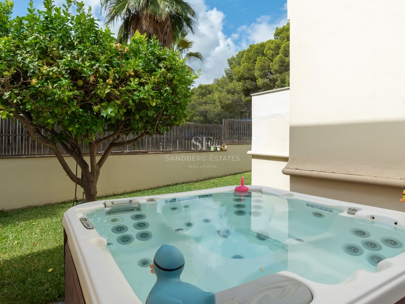 Un jacuzzi extérieur moderne dans un jardin privé à côté d'un citronnier et d'un mur blanc.