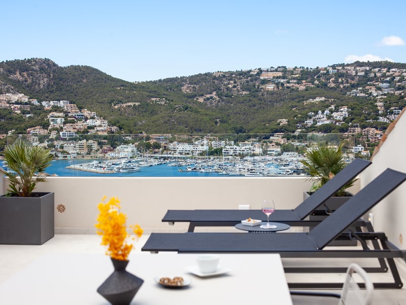 Chaises longues sur une terrasse moderne avec vue panoramique sur un port de plaisance et des collines.