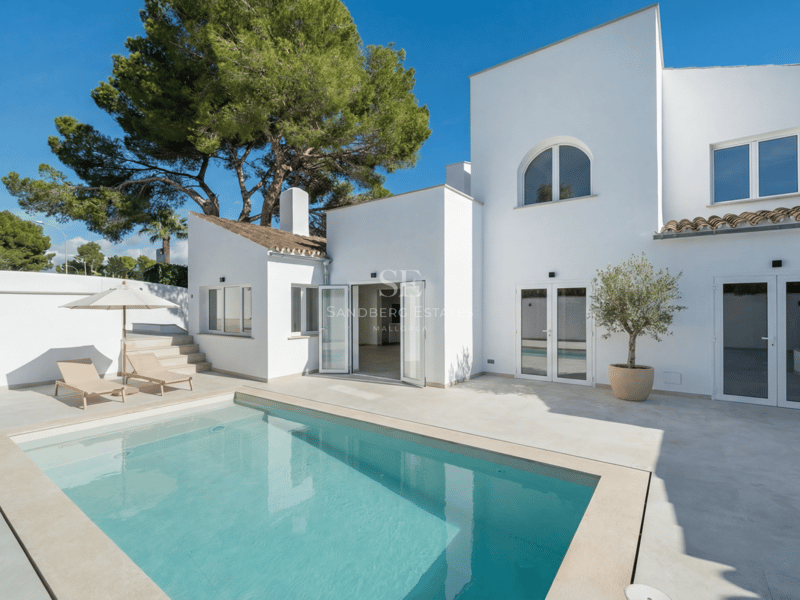 Villa blanche moderne avec piscine turquoise, terrasse en pierre et bains de soleil sous un ciel bleu clair.