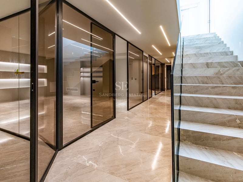 Couloir moderne avec escalier en marbre, cloisons en verre fumé et éclairage LED linéaire au plafond.