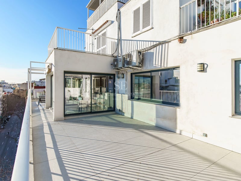 Terrasse ensoleillée avec carrelage clair, garde-corps blancs et vue sur une rue citadine sous un ciel bleu.