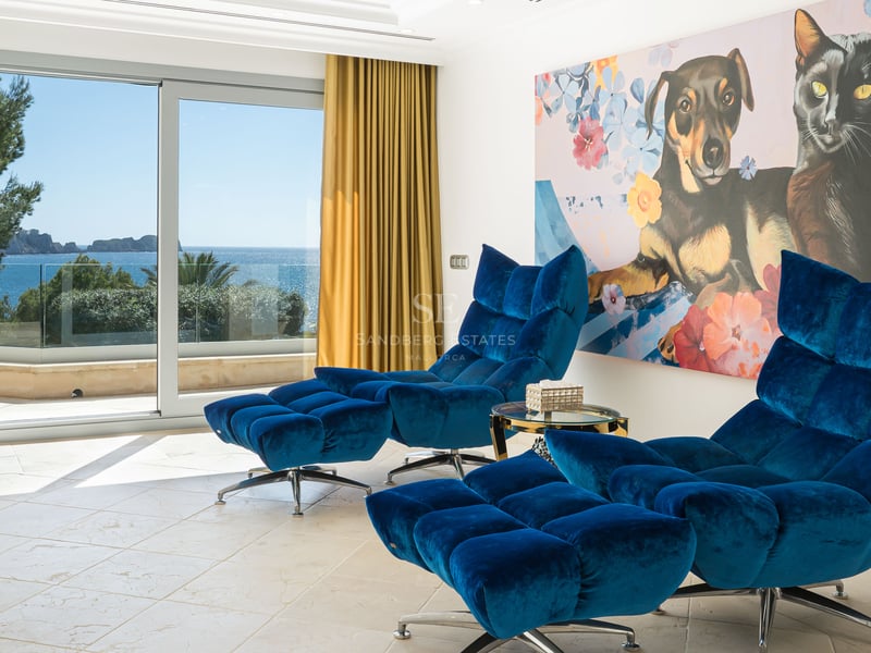 Zwei blaue Samt-Loungesessel mit Hockern in einem hellen Raum mit Blick auf das Meer durch Glasschiebetüren.