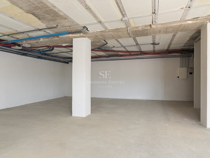 Geräumige Tiefgarage aus Beton mit freiliegenden Versorgungsleitungen und einer weißen Stützsäule.