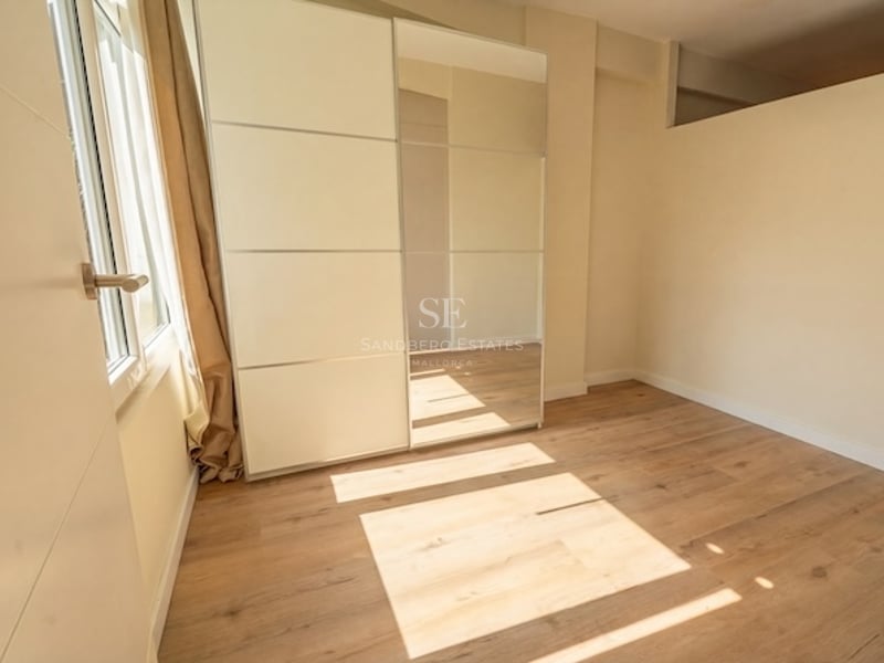 Dormitorio moderno vacío con suelo de roble claro, paredes crema y un gran armario empotrado con espejo.