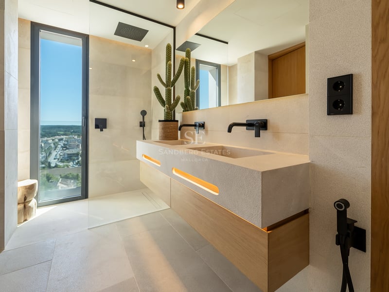 Salle de bain de luxe avec double vasque en pierre naturelle, robinetterie noir mat et grande baie vitrée.