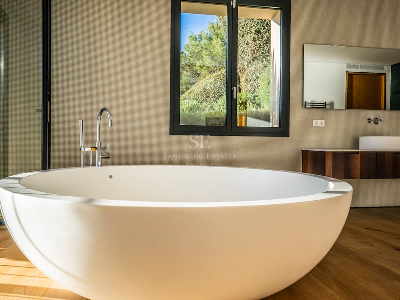 Modernes Master-Badezimmer mit großer weißer freistehender Badewanne auf Eichenparkett und Blick in den Garten.