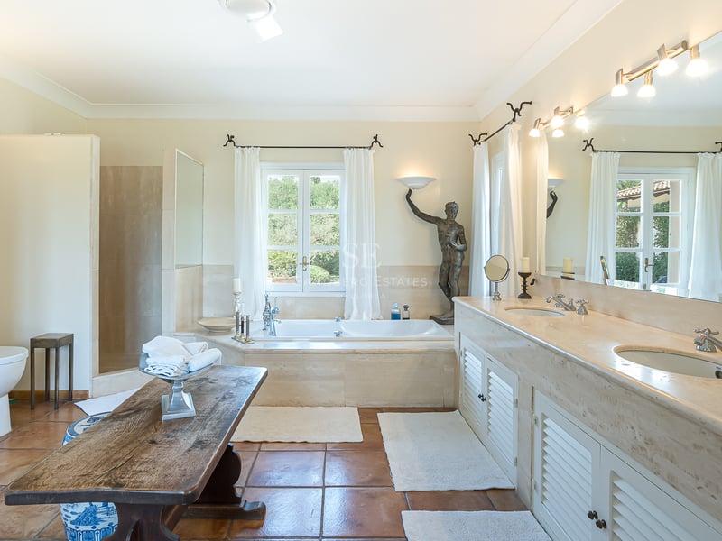 Grande salle de bain avec double vasque en marbre, baignoire sous fenêtre et sol en terre cuite.